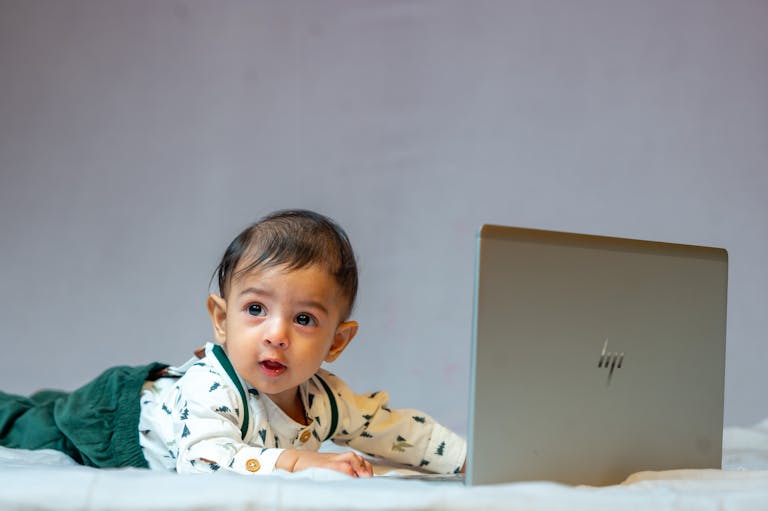A cute baby lying on bed with a laptop, exploring technology indoors.