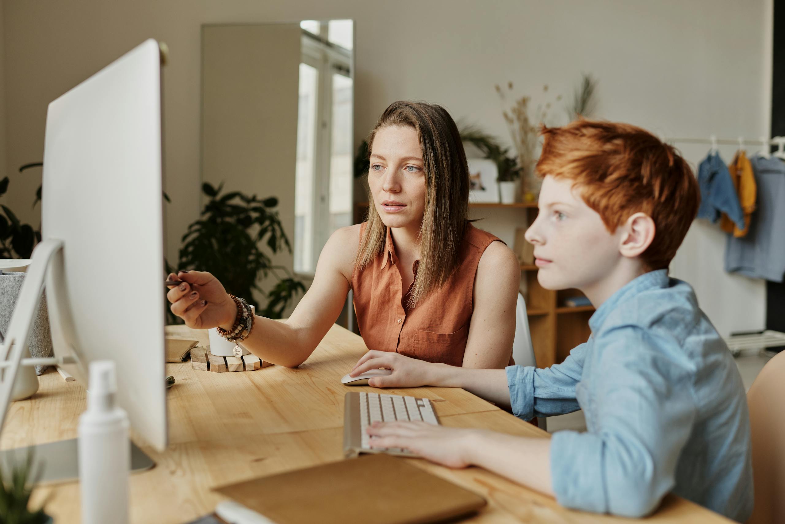 A mother and her son attentively engaged in online learning at home on a computer.