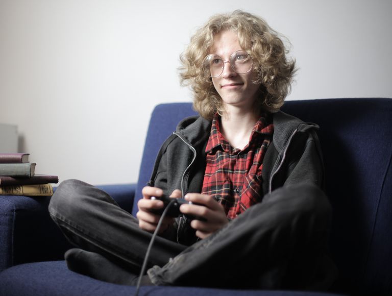 Interested youthful male in casual clothes sitting on couch and playing video games with joystick in hands while resting during weekend at home